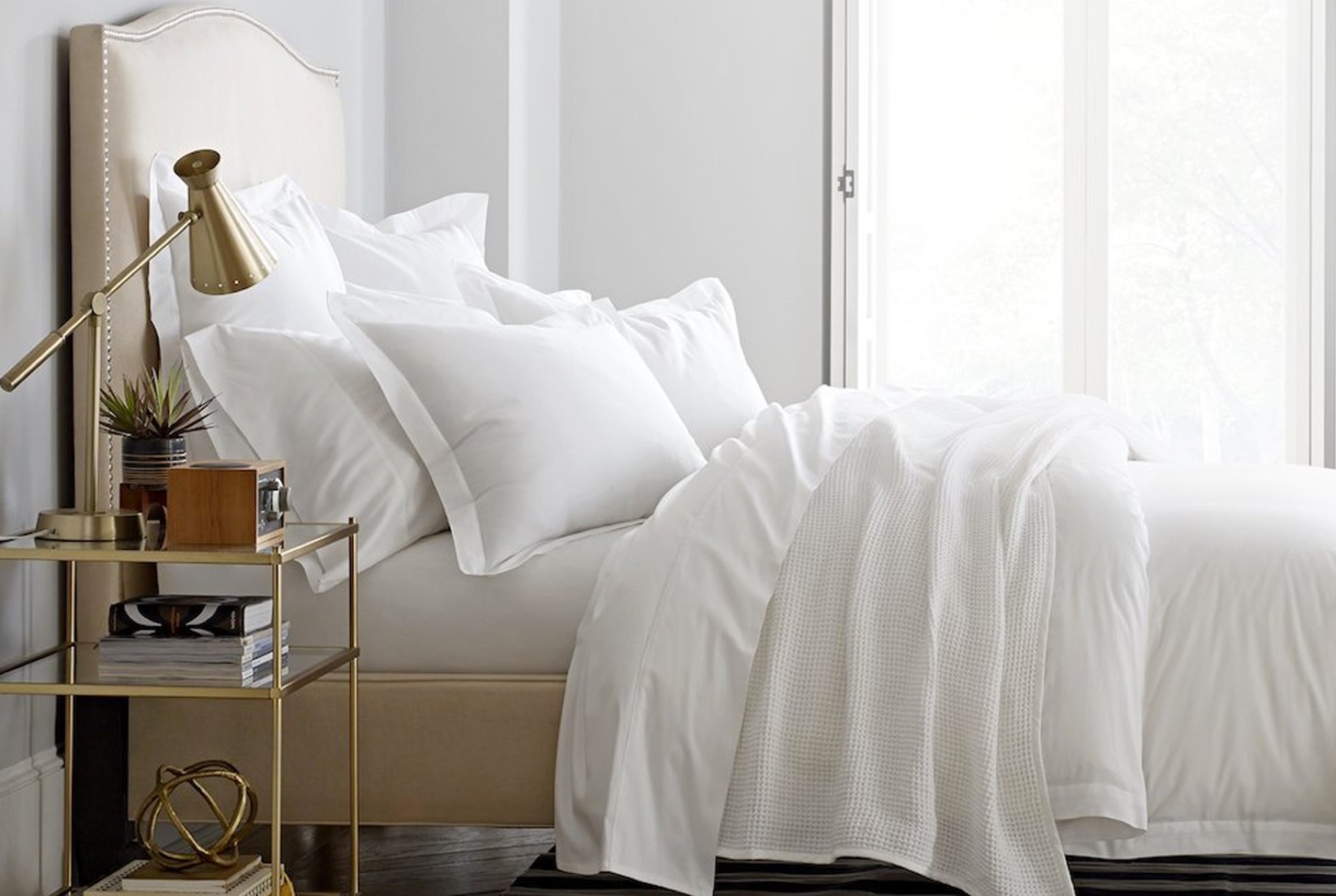 Fresh white bedsheets cover a plush mattress atop a leather-wrapped bed frame