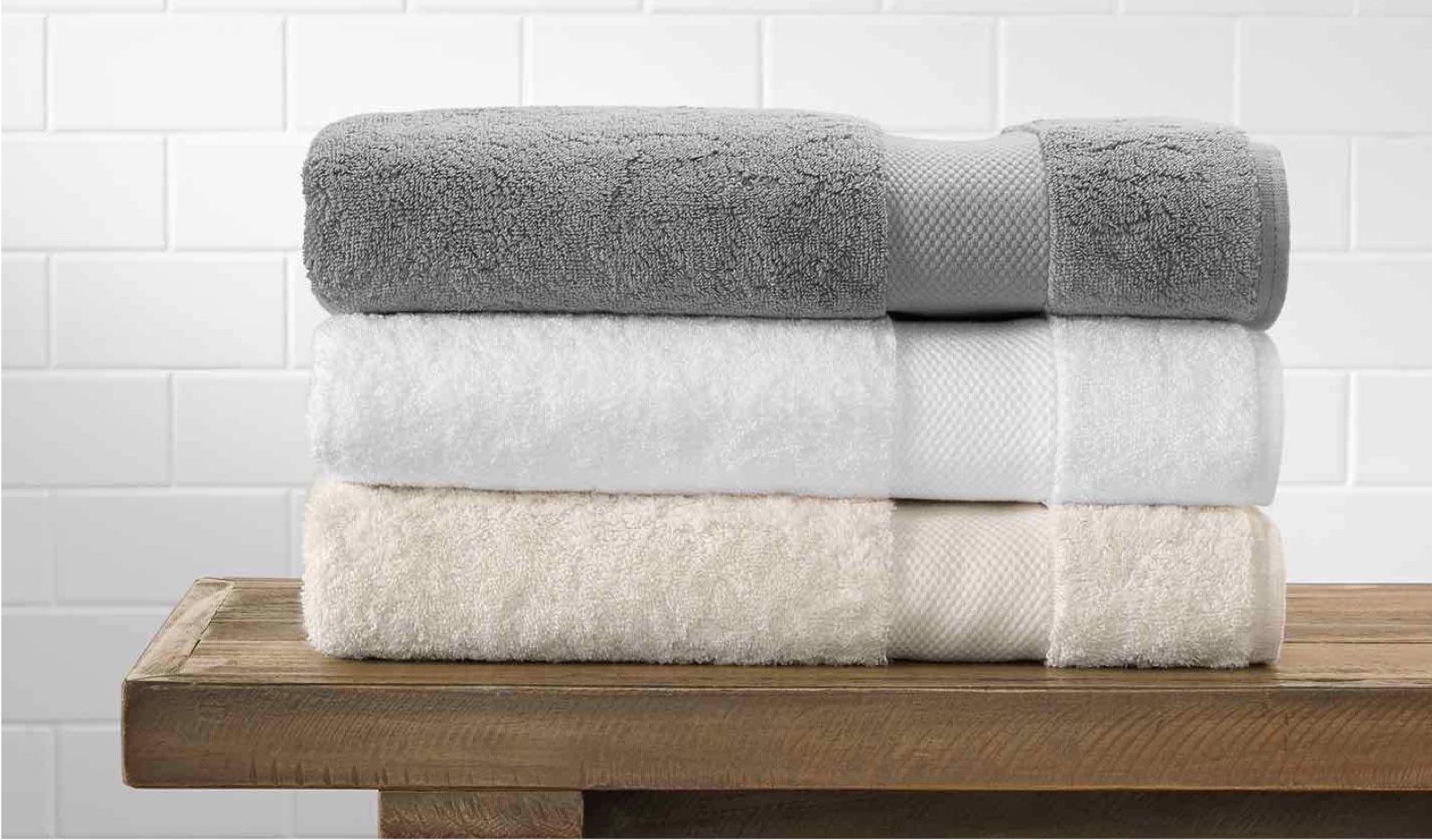 A stack of three neatly-folded towels rests upon a wooden console table