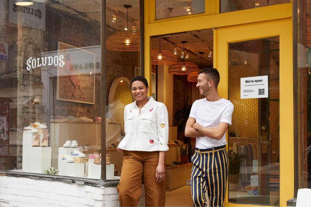 Storefront with two store owners standing in front of a door with a sign that says ’We're open’.