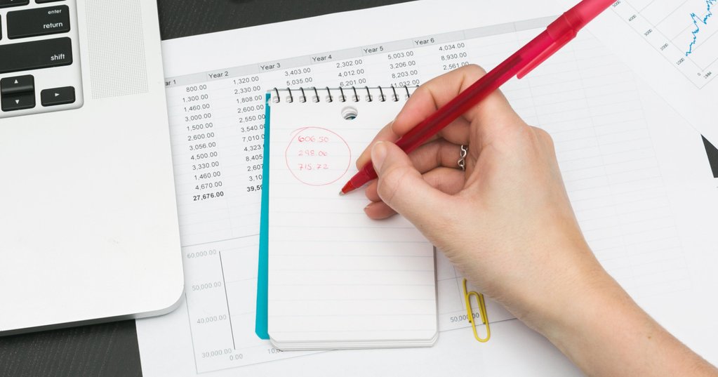 Financial planning with a laptop, charts, and a hand is writing on a notebook. 
