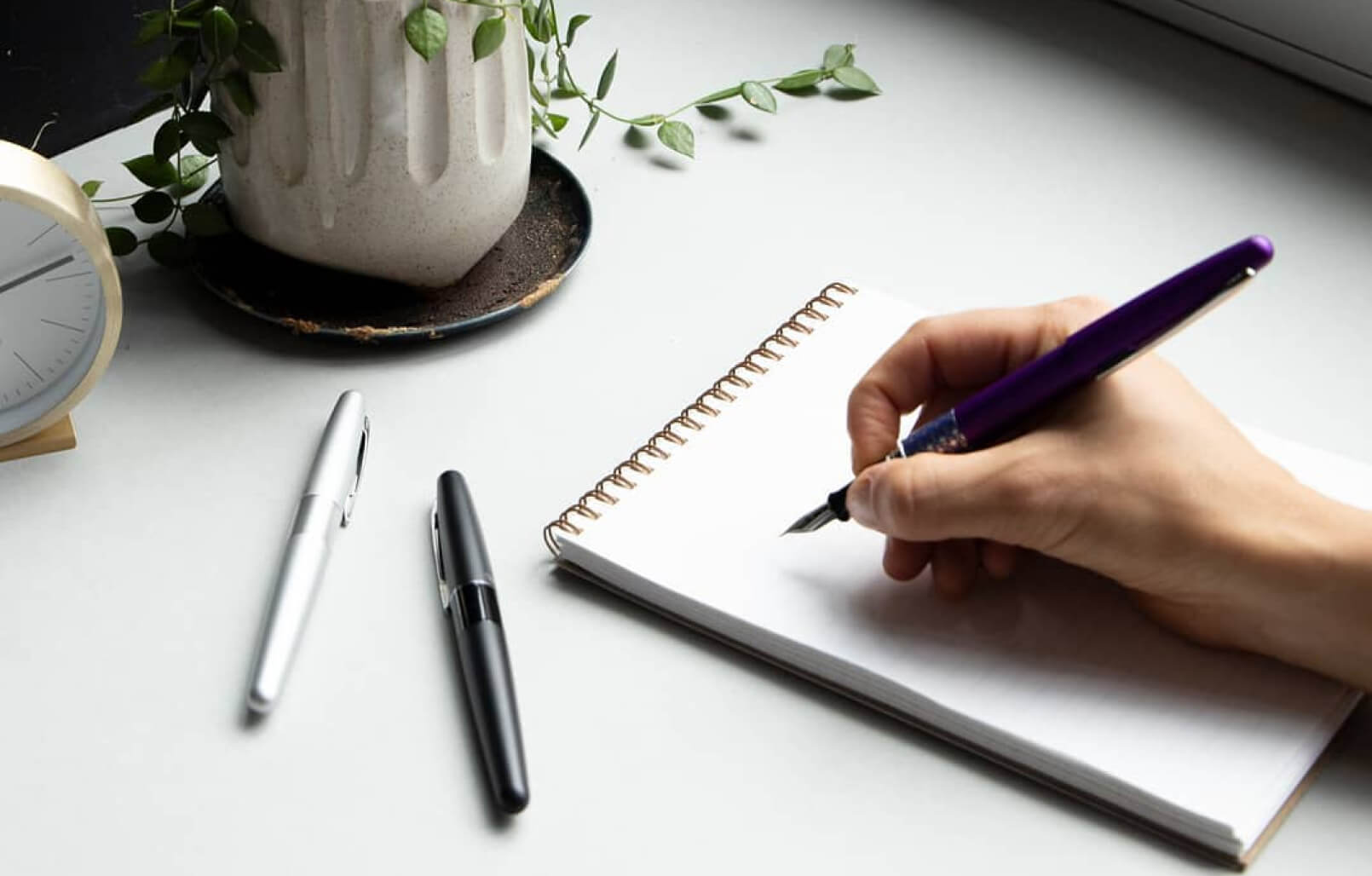 An individual ready to write something using Milligram's classic fountain pen on a notebook. With some other Milligram stationery laid out on the table.